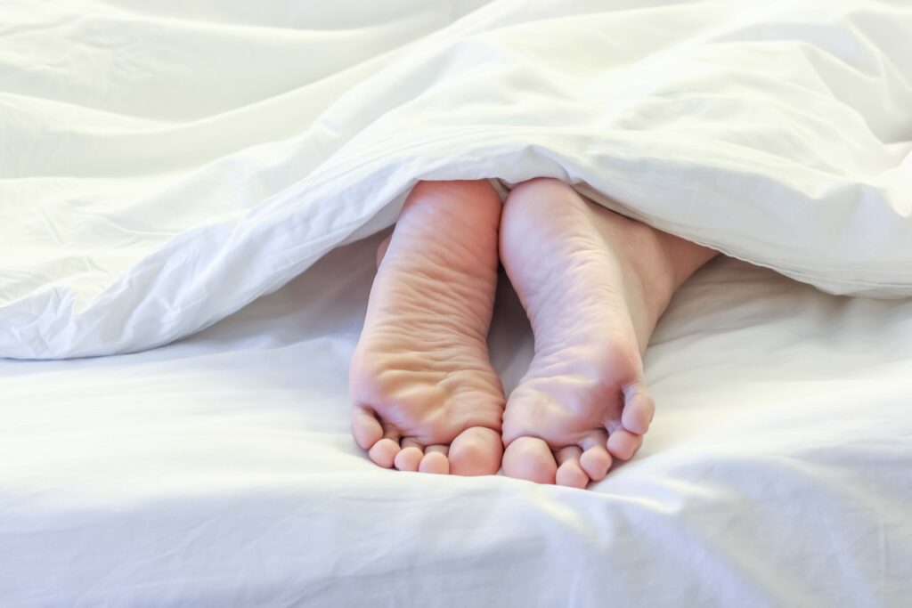 Füße einer schlafenden Frau schauen unter der weißen Bettdecke hervor