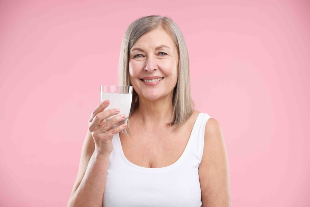 Smiling woman with glass of collagen water on pink background