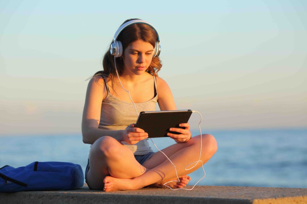 Full view portrait of a student e learning with a tablet sitting on a bench on the beach at sunset