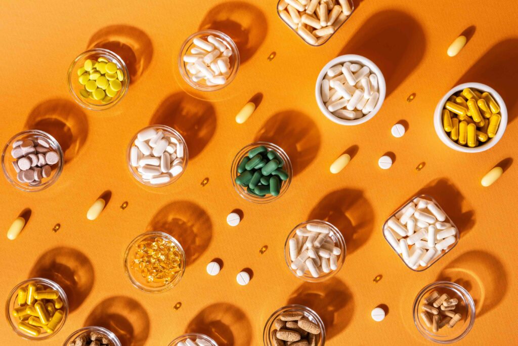Organic dietary supplements, many capsules of vitamins and minerals in small bowls from above on an orange background. Nutritional supplements, pills and tablets, top view. Healthy lifestyle.
