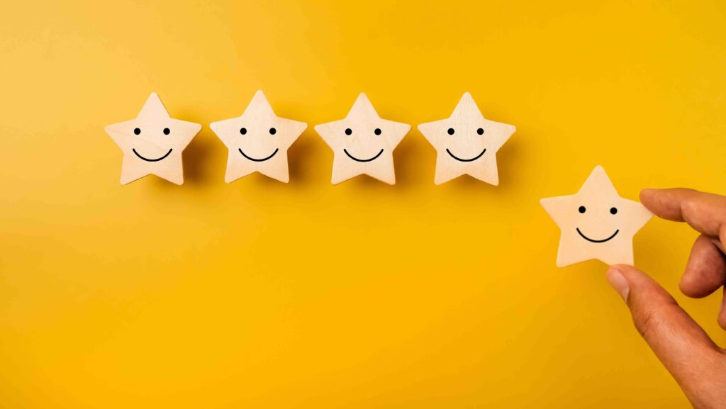 Happy smile face emoticon on stars, on yellow background and hand holding one star for more rating satisfaction. Customer evaluation, 5 rates excellence quality service, business marketing concept.