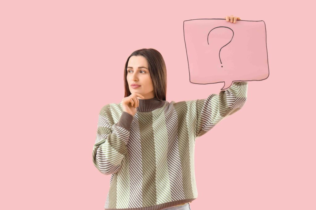 Thoughtful young woman holding speech bubble with question mark on pink background