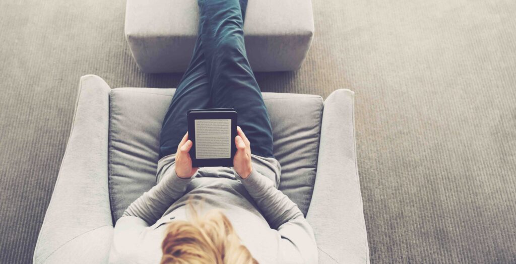 High view of a young blond man reading a book on digital device