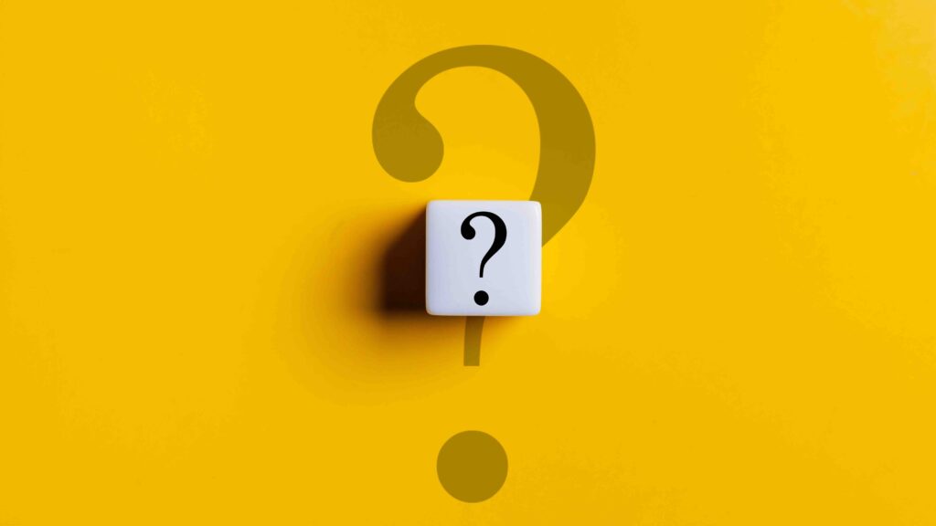 A white cube with a black question mark on it is on a yellow background. The cube is placed in the center of the image, and the question mark is pointing upwards. Concept of curiosity and intrigue