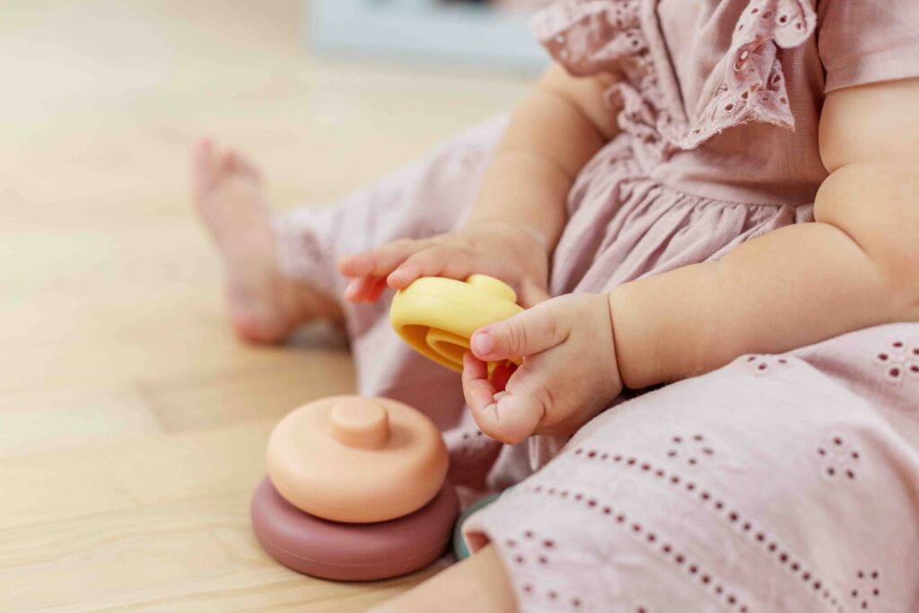 Close-up of baby’s hands holding soft pastel rings while seated on the floor, promoting fine motor skills and early learning.