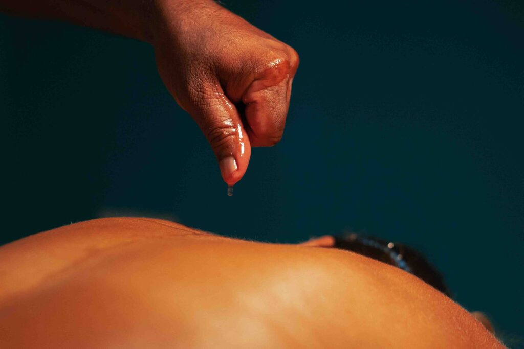  Body massage with oil under dim electric warm light in twilight and a cozy atmosphere in an Ayurvedic spa salon. An Asian man gives a massage to a European beautiful girl with tanned skin