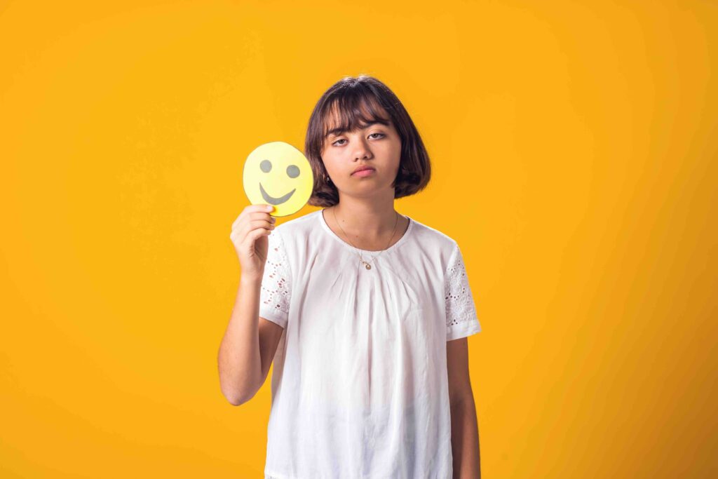 Upset girl holds happy emoticon. Stress and psychology concept