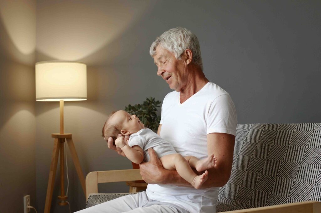 Senior man sitting calmly holding his adorable granddaughter retired grandfather wearing a white T-shirt gently cradled his newborn grandson innocent baby with granddad